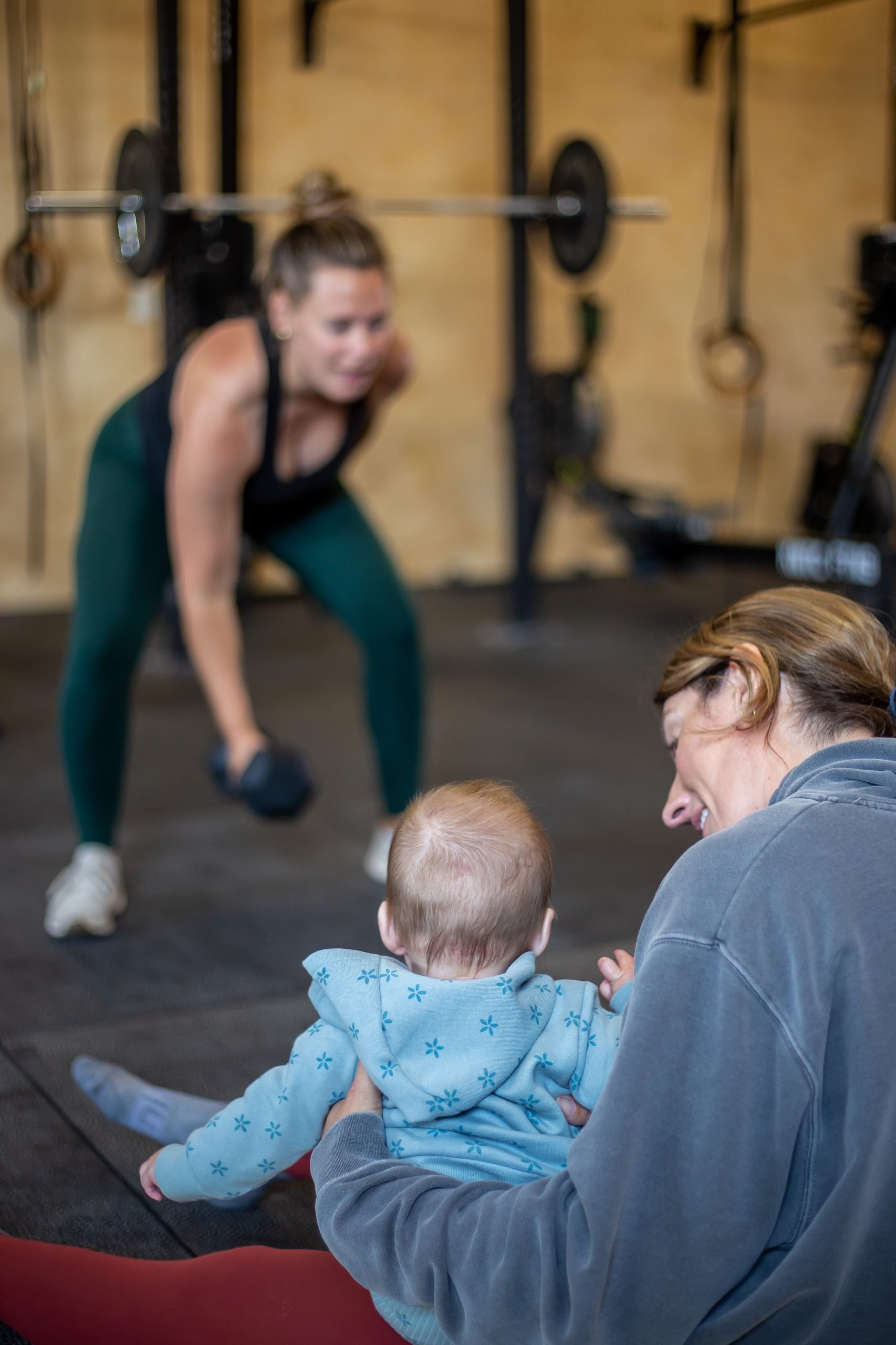 KineticPostpartum-41 Coach holding baby watching mom exercise